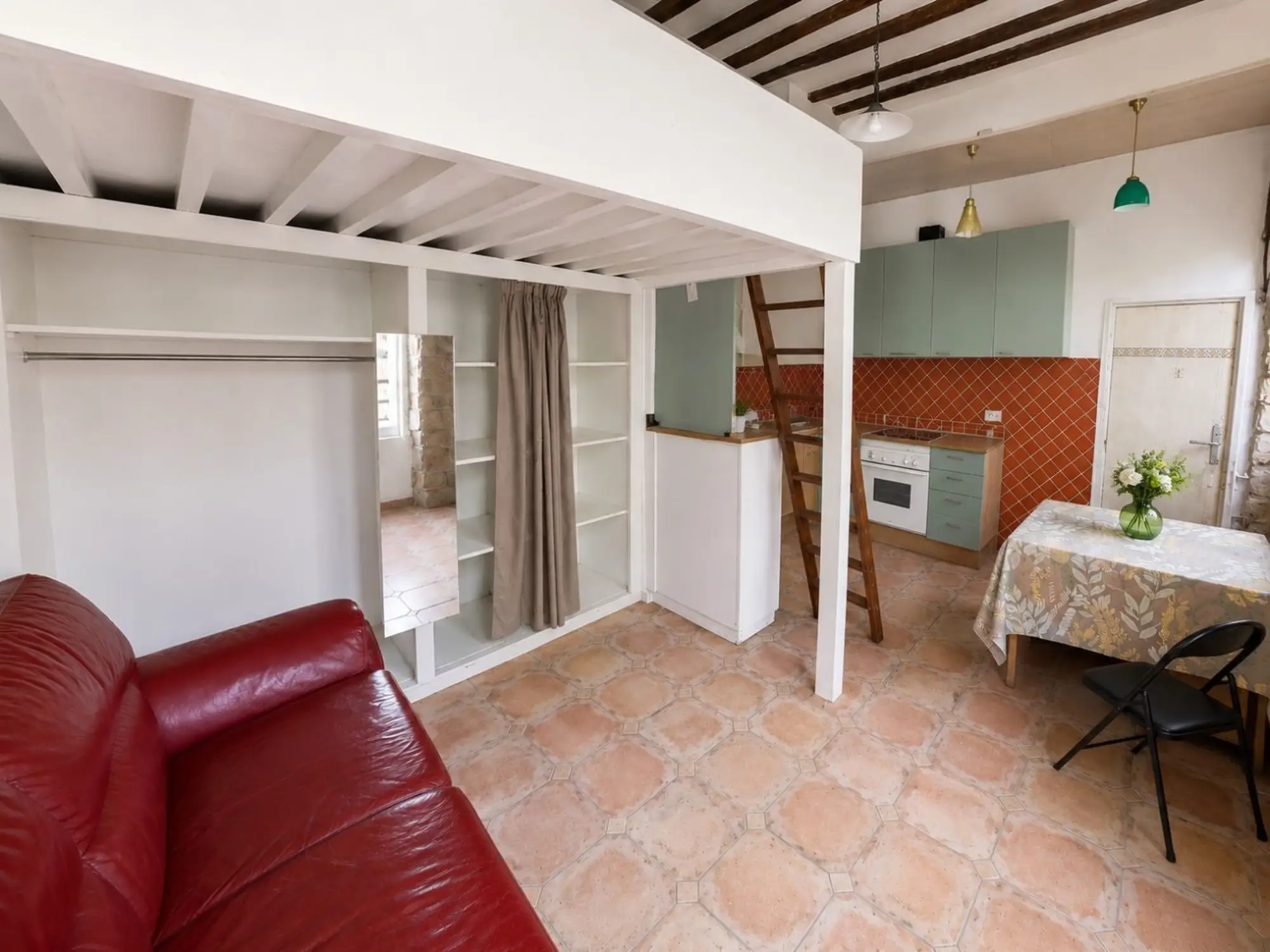 Séjour du studio avec mezzanine, cuisine ouverte et mur en pierre apparente